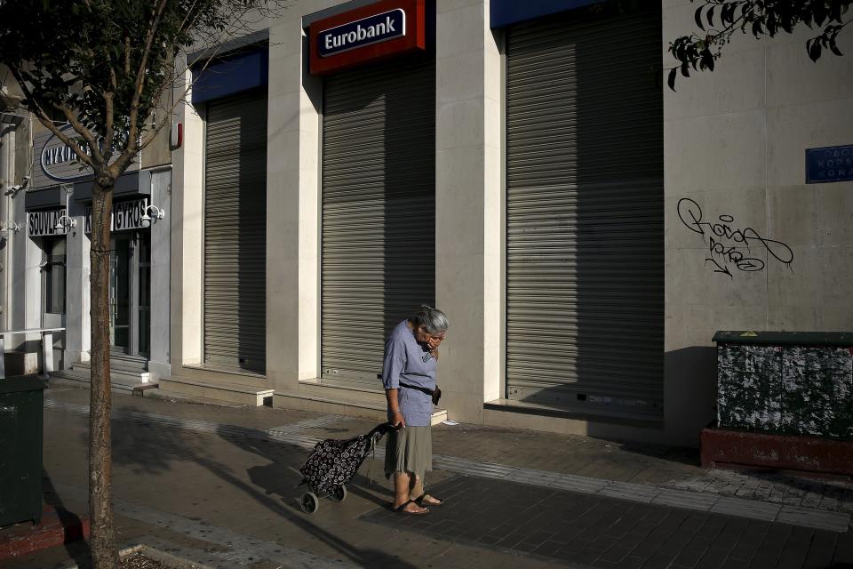 Una mujer que lleva un carrito de la compra se muestra abatida cuando pasa por delante de una sucursal bancaria cerrada.