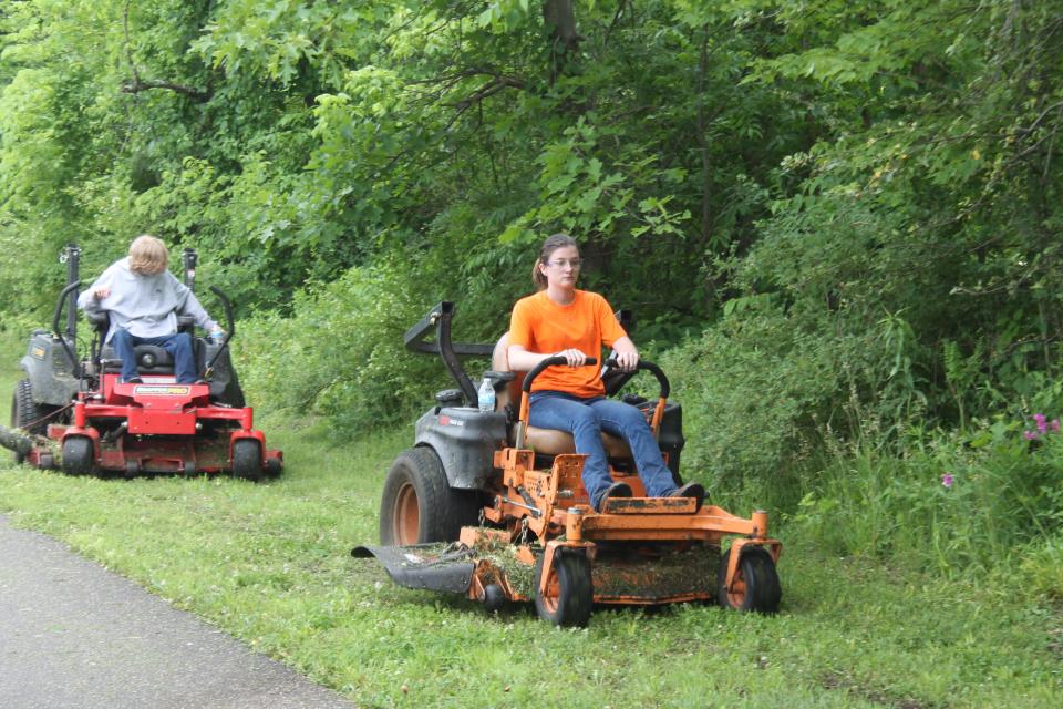 Honey West and Roger Berry, members of the summer youth workforce program, mow grass along the Great Guernsey Trail while working for the Guernsey County Community Development Corp.