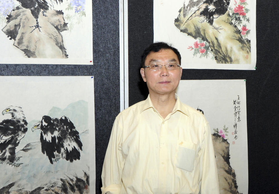 In this handout photo taken March 4, 2014 and provided March 18, 2014 by Daniel Liau, Chinese artist Wang Linshi, poses for a picture in front of pieces of his work on display at an exhibition of Chinese art in Kuala Lumpur, just days before he boarded Malaysia Airlines flight 370 to Beijing that has since gone missing. Wang, 69, worked for the Chinese government in the eastern city of Nanjing until he retired, but his passion was painting, according to son Wang Zhen. (AP Photo)