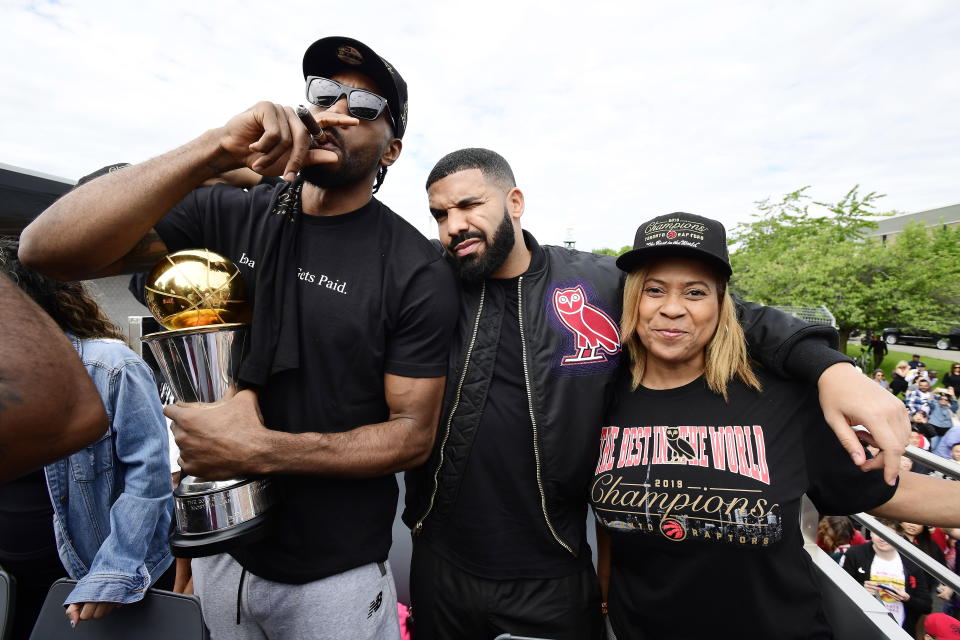 Toronto Raptors forward Kawhi Leonard, left to right, smokes a cigar holding his playoffs MVP trophy as he celebrates with performing artist Drake and his mother Kim Robertson during the 2019 Toronto Raptors NBA basketball championship parade in Toronto, Monday, June 17, 2019. (Photo by Frank Gunn/The Canadian Press via AP)