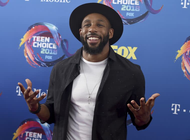 A man wearing a hat smiles while holding his hands out