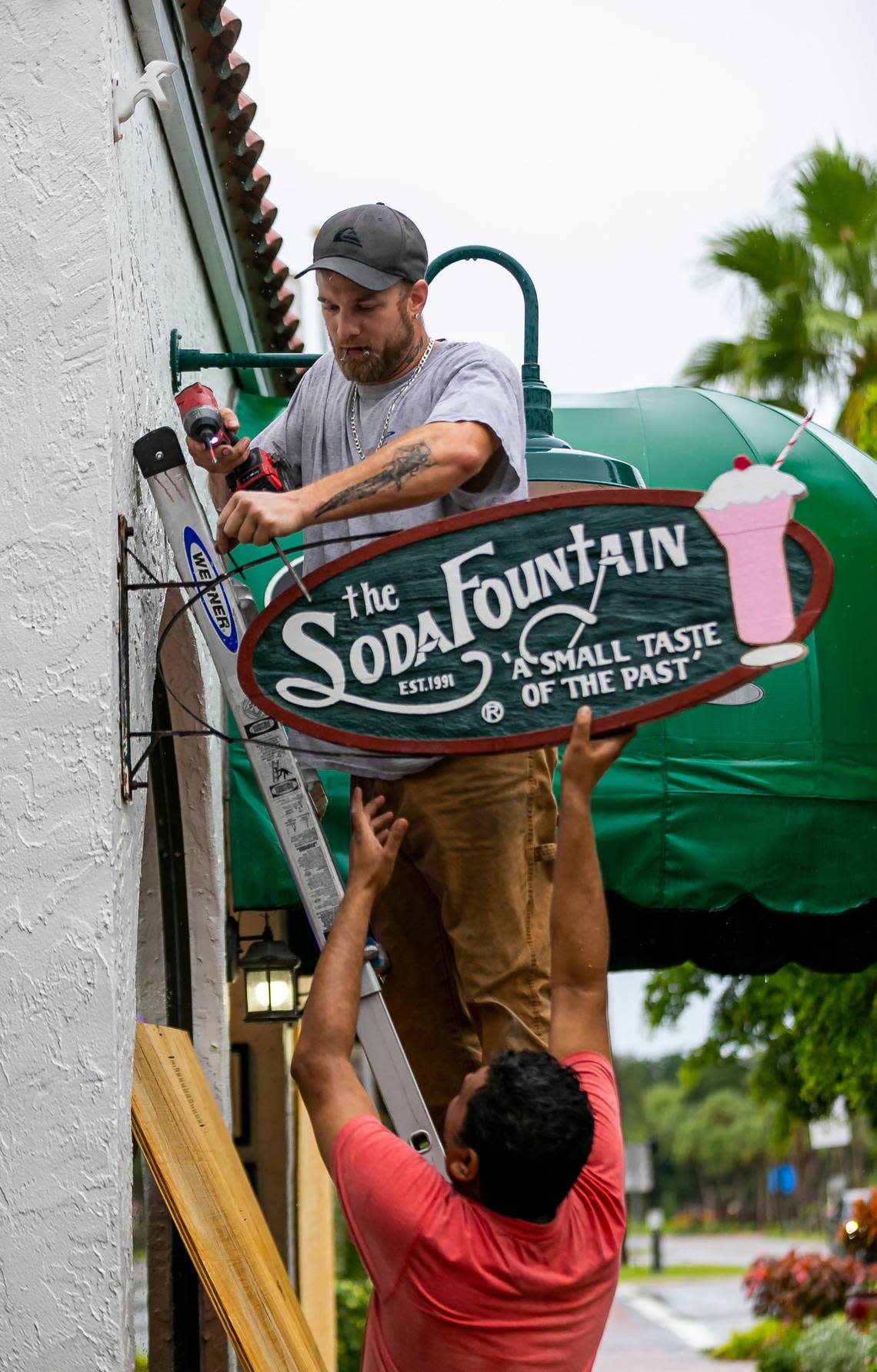 Justin Short, 35, above, and Nick Patel, 38, work to place shutters on their restaurant, the Soda Fountain of Venice, on Tuesday, Sept. 27, 2022, in Venice, Fla. Venice residents are preparing for the impacts of Hurricane Ian.