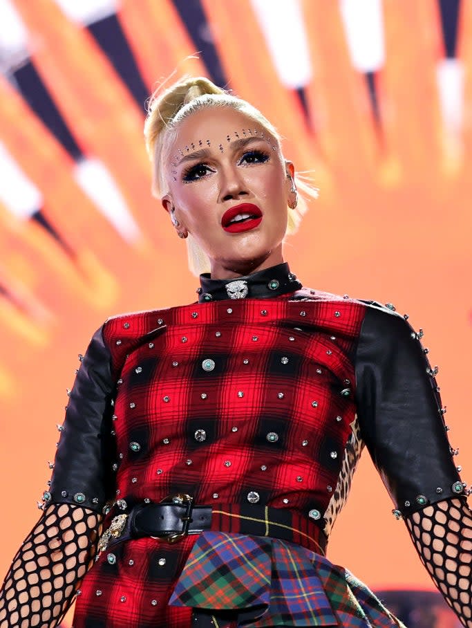 Gwen Stefani performing on stage in a plaid outfit with mesh details and bold makeup