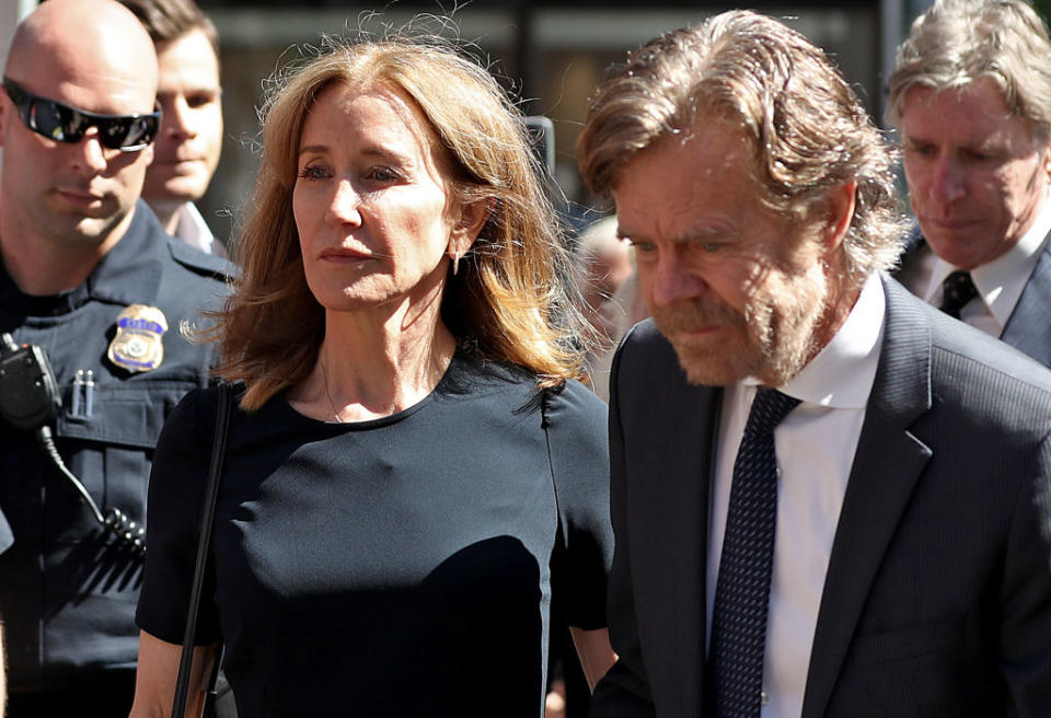 Felicity Huffman in a short-sleeved dress and William H. Macy in a suit walk together while surrounded by police officers and other people in suits