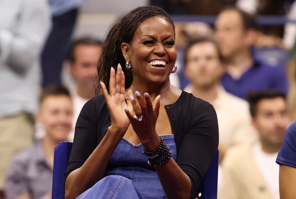 A Black woman laughs and claps. People are sitting behind her, some smiling. . 