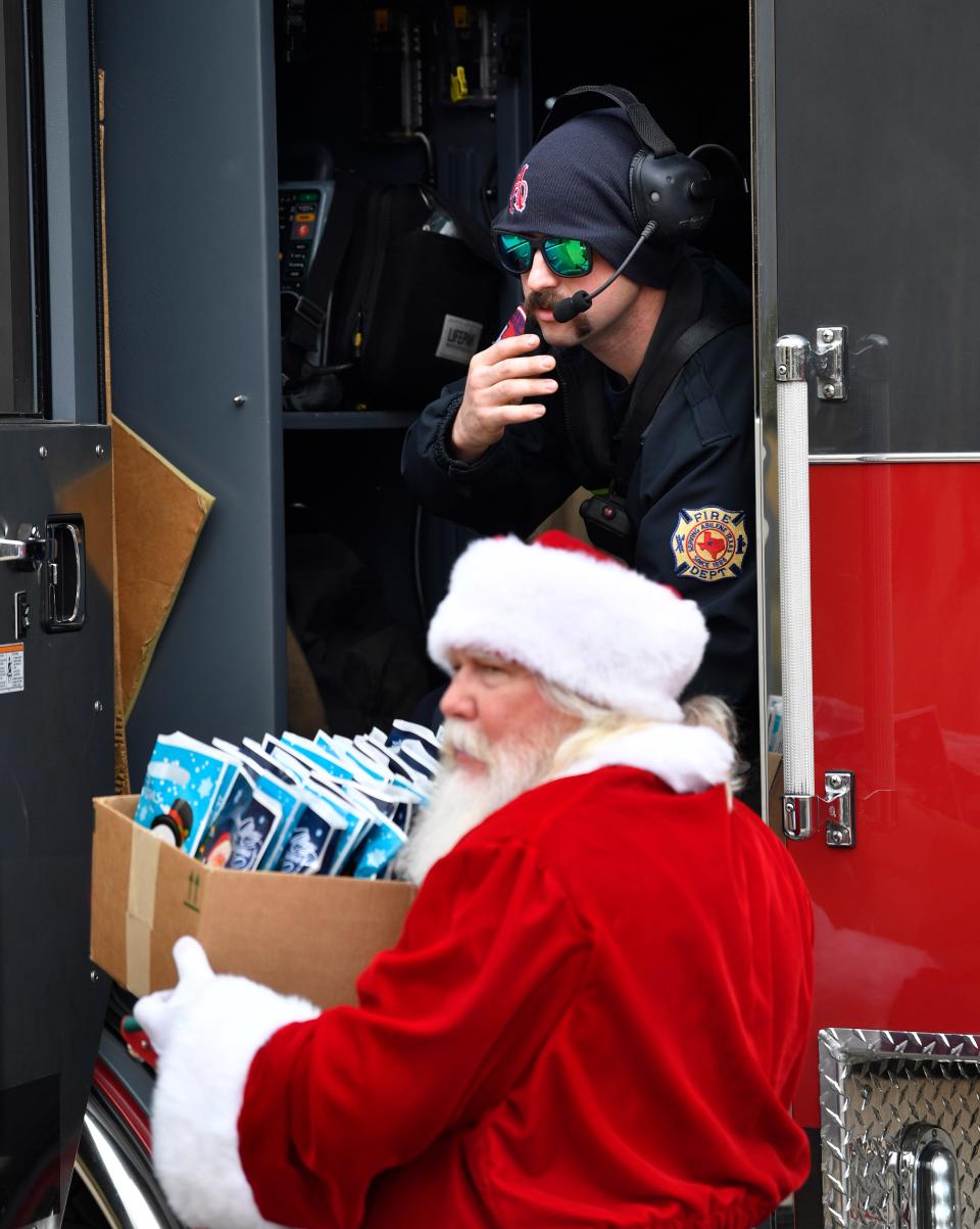 One of Santa Claus' "helpers" hands him a box of gift bags as he arrives at the Mall of Abilene in Abilene Fire Department's Ladder 8.