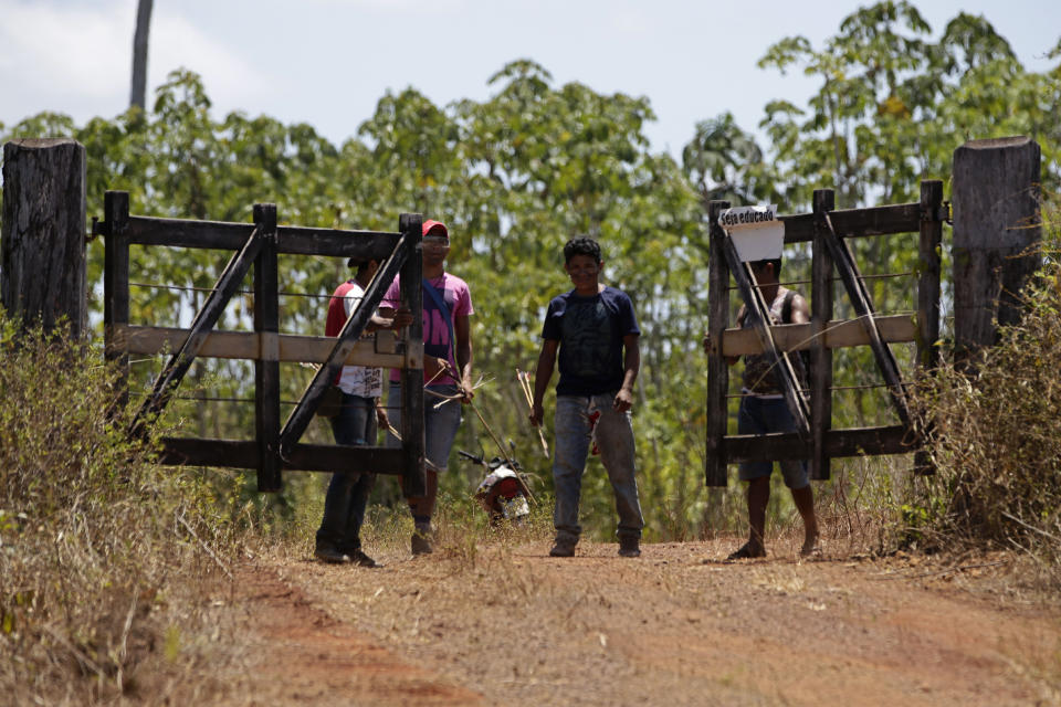 Tenetehara Indigenous men Ronilson Seleiro Tembe, center, and Regis Tufo Moreira Tembe, right, open a gate that leads to the Alto Rio Guama Indigenous Territory, where they have enforced six months of isolation during the COVID-19 pandemic, near the city of Paragominas, state of Para, northern region of Brazil, Monday, Sept. 7, 2020. The Indigenous group, also known as Tembe, held a festival this week to celebrate and give thanks that none of their members have fallen ill with COVID-19, after closing their area off in March. (AP Photo/Eraldo Peres)