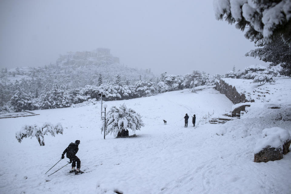 A man skis on snowy Pnyx hill in front the ancient Acropolis hill, near the ruins of the fifth century BC Parthenon temple, in Athens, Tuesday, Feb. 16, 2021. Unusually heavy snowfall has blanketed central Athens, with authorities warning residents particularly in the Greek capital's northern and eastern suburbs to avoid leaving their homes. (AP Photo/Petros Giannakouris)