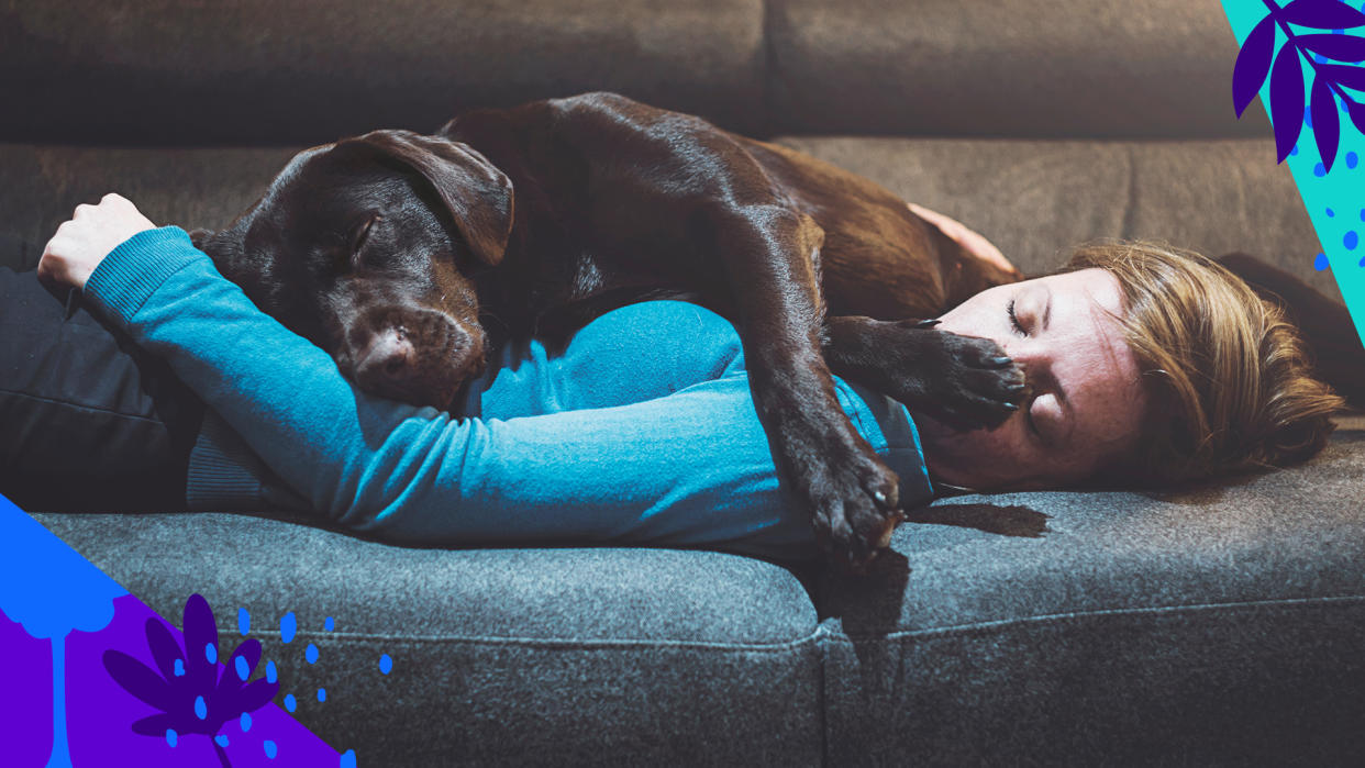 A woman lies on a couch with a black lab.