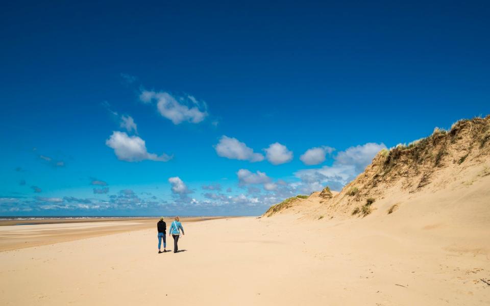 Two people enjoy a walk along the sandy beach on the coast of north-west England under a deep blue summer sky