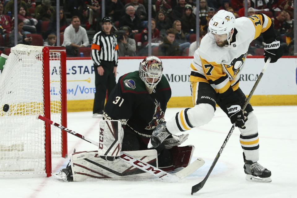 Arizona Coyotes goaltender Adin Hill (31) makes a save on a shot as Pittsburgh Penguins right wing Bryan Rust (17) gets out of the way of the shot during the second period of an NHL hockey game Sunday, Jan. 12, 2020, in Glendale, Ariz. (AP Photo/Ross D. Franklin)