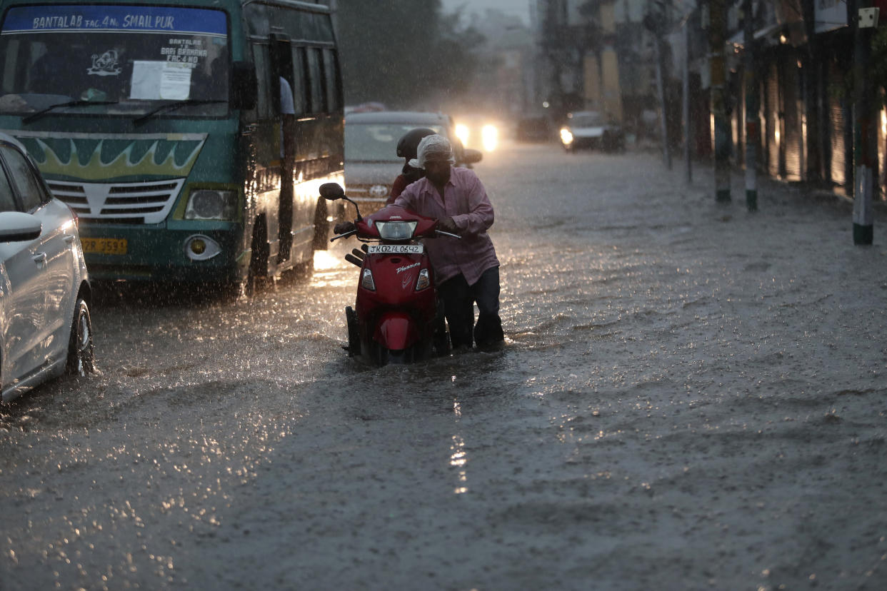 A man pushes a two wheeler through a flooded street during monsoon rains Jammu, India, Monday, July 12, 2021. India’s monsoon season runs from June to September. (AP Photo/Channi Anand)