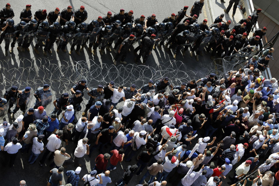 Riot police stand guard as retired Lebanese soldiers try to remove a barbed wire barrier to advance towards the government building during a protest, in Beirut, Lebanon, Monday, May 20, 2019. Lebanese security forces have opened heavy water cannons on anti-austerity protests in the capital city, as the government faces a looming fiscal crisis. Over one hundred protesters gathered Monday outside the Government House in downtown Beirut shouting "Thieves, thieves!" as the Cabinet met for its 16th session to reach agreement on controversial budget cuts. (AP Photo/Bilal Hussein)