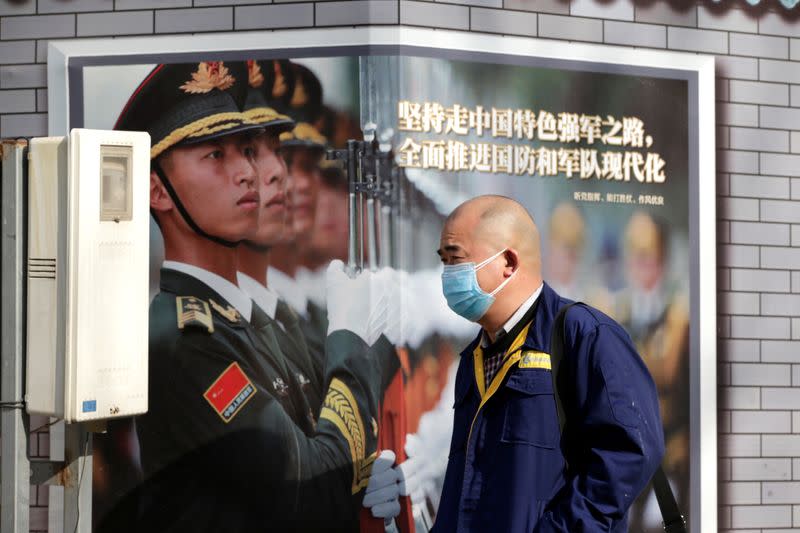 Man wearing a mask walks past a military poster at the Financial Street in central Beijing