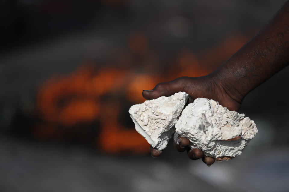 A protestor holds rocks while walking in front of burning tires at a barricade, as protesters seek to paralyze transport and commerce in order to pressure President Jovenel Moise to resign, in Port-au-Prince, Haiti, Tuesday, Oct. 8, 2019. The U.N.'s Mission for Justice Support in Haiti has urged the government to ensure the normal functioning of schools, hospitals and emergency services and allow aid to reach the most vulnerable people. (AP Photo/Rebecca Blackwell)