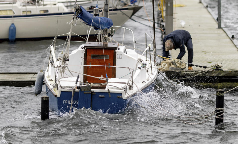 A man secures a sailboat at a jetty on the Kiel Fjord against an expected storm surge, in Kiel, Germany, Thursday Oct. 19, 2023. (Axel Heimken/dpa via AP)