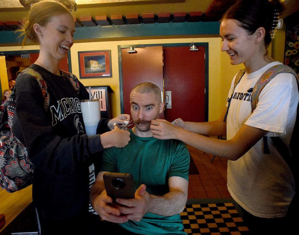 River Raisin Ballet Company dancers Evelyn Short, 18, (left) and Elora Russell, 17, who are splitting the role of Cinderella, cut off Josh Moller's moustache handlebars on April 16. Moller is playing the role of a stepsister in the production of "Cinderella" at the River Raisin for the Arts.