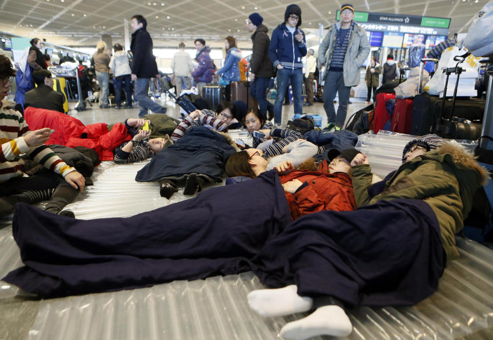 Travelers take a rest on a floor at departure lobby at Narita airport in Narita, near Tokyo Tuesday, Jan. 15, 2013 as they stayed overnight due to heavy snow. This winter's first snow in Tokyo on Monday severely disrupted train services, canceled flights and stranded tourists. (AP Photo/Kyodo News) JAPAN OUT, MANDATORY CREDIT, NO LICENSING IN CHINA, HONG KONG, JAPAN, SOUTH KOREA AND FRANCE