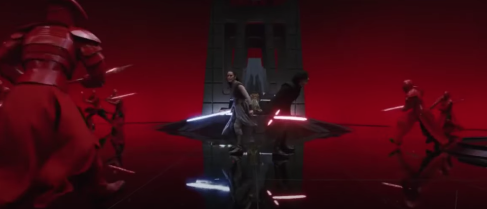 A man and a woman wield lightsabers, prepared to fight back to back