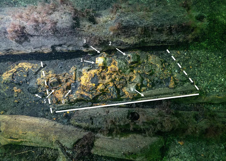 The weapons chest found. The lines show the estimated sides of the chest. The contents include lead plates (1), molds (2 and 3), and the cans that may have contained powder (5).  / Credit: Photo by Florian Huber, outlines and notes by Rolf Warming