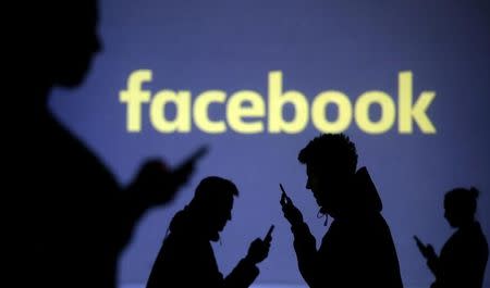 Silhouettes of mobile users are seen next to a screen projection of Facebook logo in this picture illustration taken March 28, 2018. REUTERS/Dado Ruvic/Illustration
