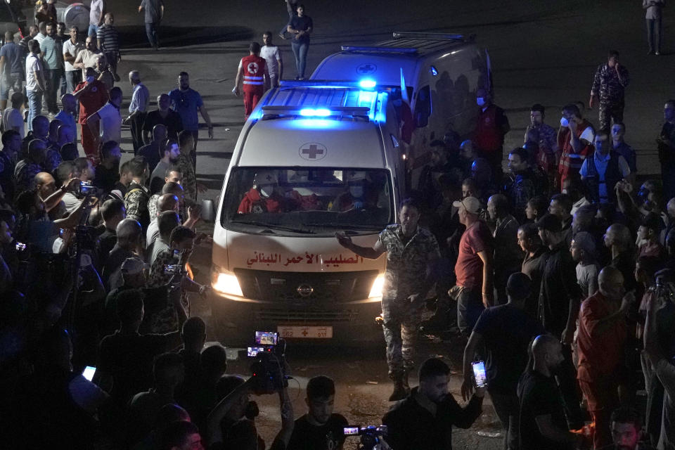 People gathering around Lebanese Red Cross ambulances that carrying dead bodies of those who were on a boat carrying migrants from Lebanon that sank in Syrian waters, as they cross a border point between Lebanon and Syria, in Arida, north Lebanon, Sept. 23, 2022. Syria's health minister says several people have been killed from a boat that sank migrants from Lebanon off Syria's coast. The incident is the deadliest since a surging number of Lebanese, Syrians, and Palestinians have tried to flee crisis-hit Lebanon by sea to Europe. (AP Photo/Bilal Hussein)