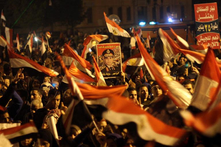 Egyptians wave the national flag and hold up pictures of army chief Abdel Fattah al-Sisi during a gathering in General Abdel Monim Riyad square at the edges of Cairo's Tahrir square on January 25, 2014