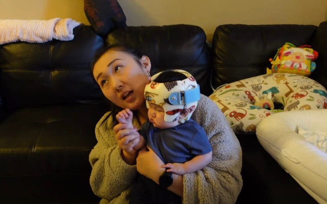 A mother holds her very young child, who is wearing one of the helmets