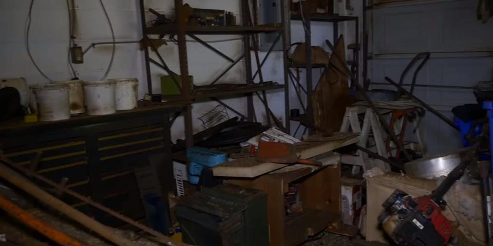 A dark, dirty garage crowded with items, such as shelves and old appliances.