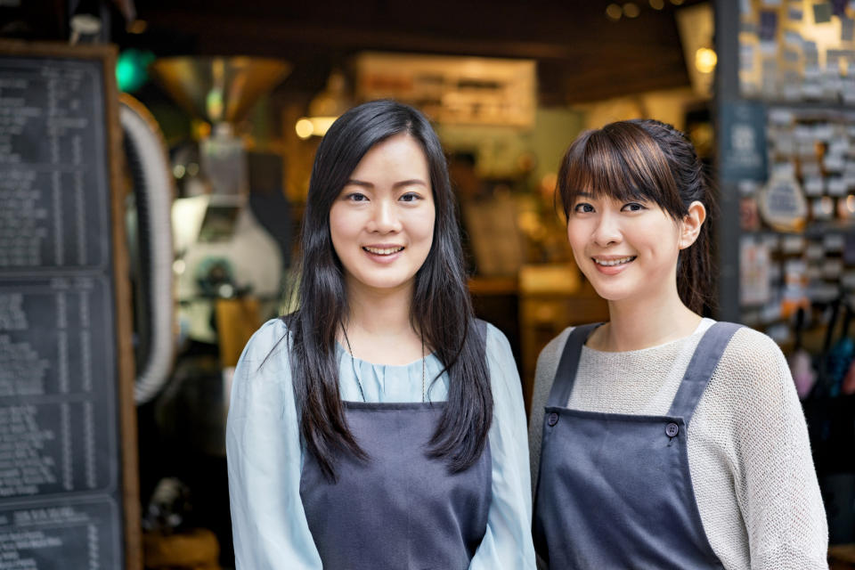 Portrait of smiling female cafe workers standing against coffee shop.