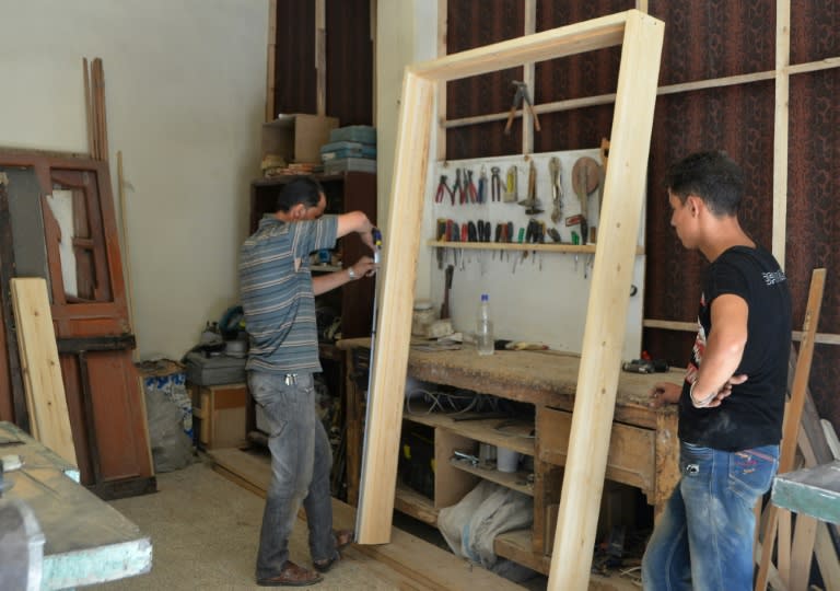 Syrian furniture maker Hussam Obayd and an assistant measure wood in his Saqba workshop