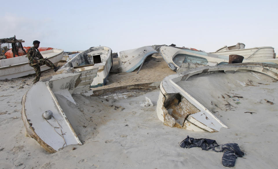 In this photo taken Sunday, Sept. 23, 2012, a Somali government soldier walks next to some of the overturned pirate skiffs that litter the dunes on the shoreline near the once-bustling pirate den of Hobyo, Somalia. The empty whisky bottles and overturned, sand-filled skiffs that litter this shoreline are signs that the heyday of Somali piracy may be over - most of the prostitutes are gone, the luxury cars repossessed, and pirates talk more about catching lobsters than seizing cargo ships. (AP Photo/Farah Abdi Warsameh)
