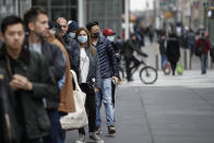 FILE - In this Friday, March 20, 2020 file photo, customers wearing protective face masks to protect against the coronavirus, wait in line outside a Whole Foods supermarket on 6th Avenue, in New York. A pandemic forcing everyone to stay home could be the perfect moment for online grocery services. In practice, they've been struggling to keep up with a surge in orders, highlighting their limited ability to respond to an unprecedented onslaught of demand. After panic buying left store shelves stripped of staples like pasta, canned goods and toilet paper, many shoppers quickly found online grocery delivery slots almost impossible to come by, too. (AP Photo/John Minchillo, File)