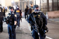 A Department of Homeland Security officer stands watch as fellow officers extinguish a fire lit by protesters behind the Mark O. Hatfield United States Courthouse on Sun, Aug. 2, 2020, in Portland, Ore. Following an agreement between Democratic Gov. Kate Brown and the Trump administration to reduce federal officers in the city, nightly protests remained largely peaceful without major confrontations between protesters and officers. (AP Photo/Noah Berger)