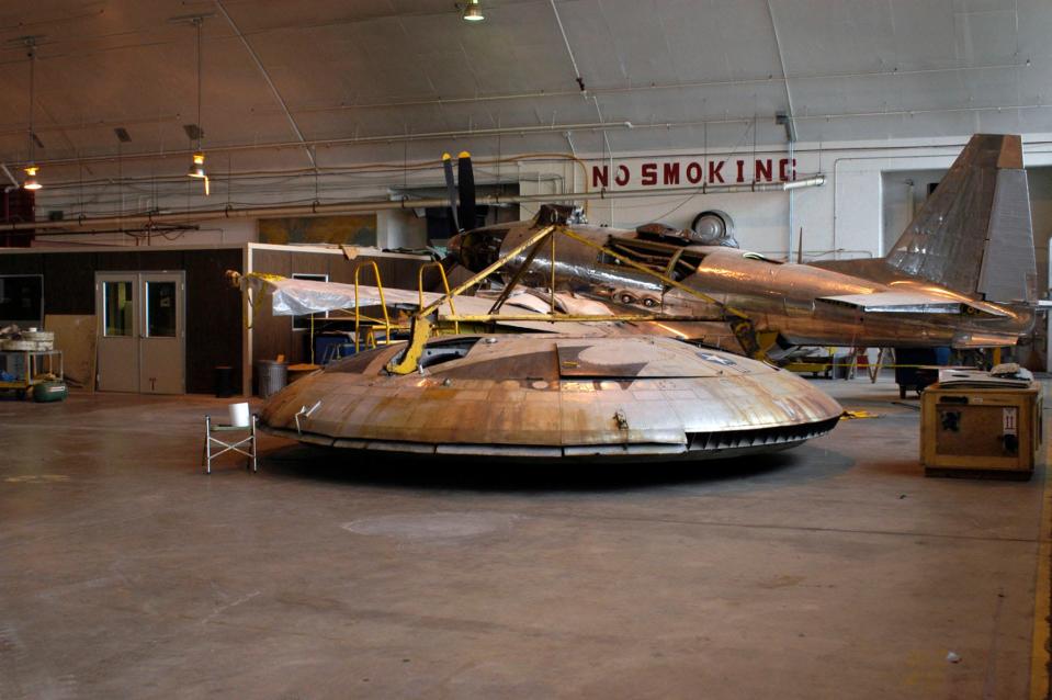 A photo of the Avrocar sitting among other old air crafts in the restoration hangar.