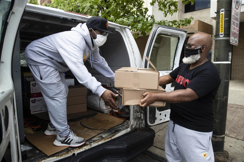 Pas Simpson, left, and Hasshan Batts, right, of Promise Neighborhoods of the Lehigh Valley, a community group, load a truck with hot meals for delivery to people in need in Allentown, Pa., Friday, May 29, 2020. The Allentown community group's executive director Batts and his colleagues also began buying up all the diapers they could find - 60,000 and counting - and have been going door to door to distribute them to families in need. (AP Photo/Matt Rourke)