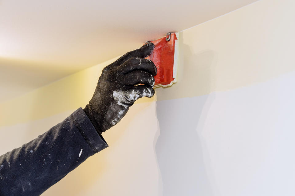 A person using a paint edger along the top of a wall