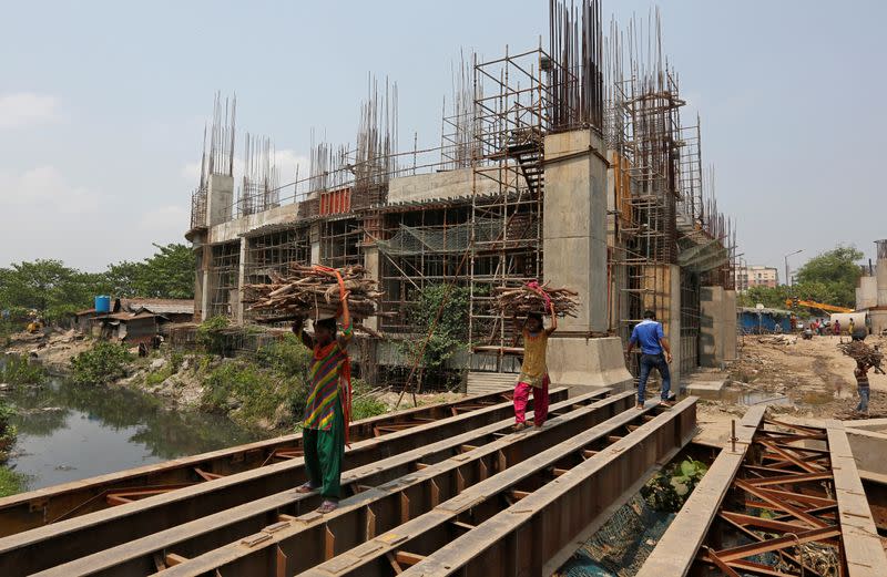 Women carry firewood on iron beams laid over a canal next to the construction site of a metro rail station in Kolkata