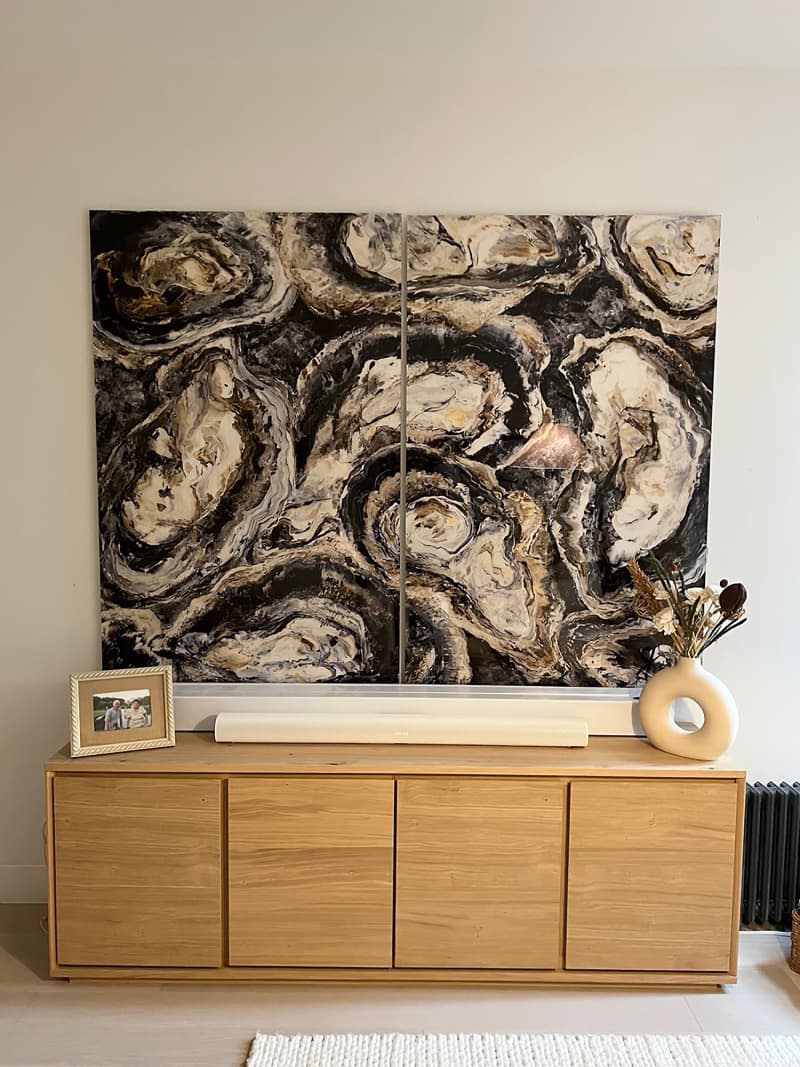 Oyster diptych artwork hung on beige wall above wood sideboard cabinet with vase and framed photo.