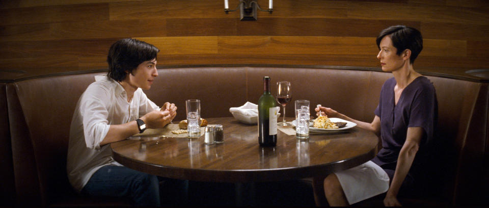 Tilda Swinton and Ezra Miller sit at a table eating a meal