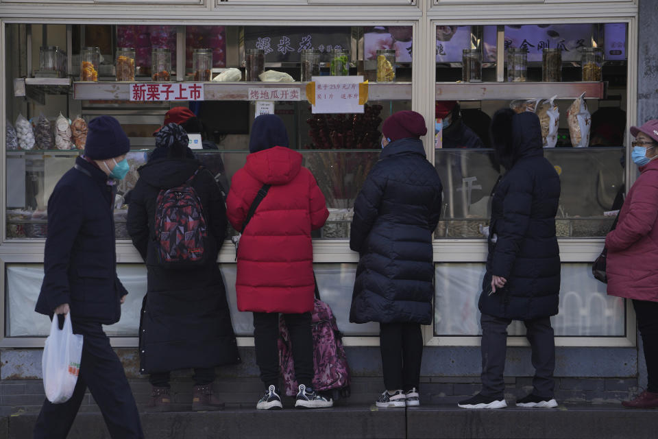 A resident wearing a face mask walks by women who line up to buy snack foods at a store in Beijing, Tuesday, Jan. 17, 2023. China’s economic growth fell to 3% last year under pressure from antivirus controls and a real estate slump but is gradually reviving after restrictions that kept millions of people at home were lifted. (AP Photo/Andy Wong)