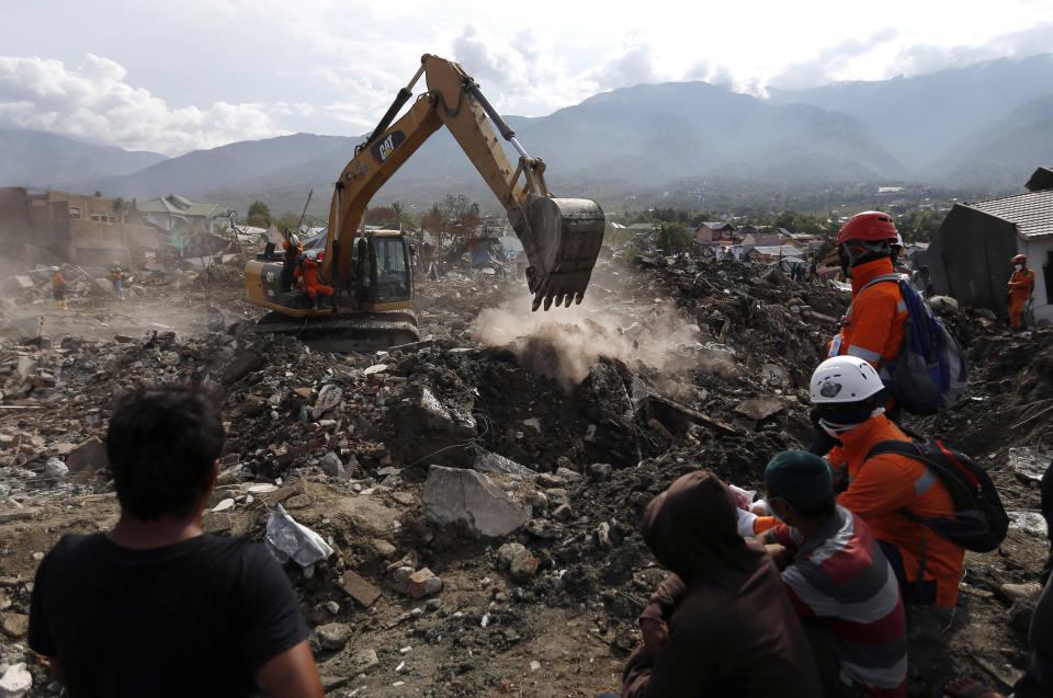 FILE - In this Thursday, Oct. 11, 2018, file photo, rescue workers watch as a heavy machine dig through rubble searching for earthquake victims at Balaroa neighborhood in Palu, Central Sulawesi, Indonesia, Thursday, Oct. 11, 2018. Indonesia's disaster agency says helicopters are dropping disinfectant on neighborhoods in the earthquake and tsunami-stricken city of Palu to reduce disease risks from the thousands of victims believed buried in obliterated communities. (AP Photo/Dita Alangkara, File)