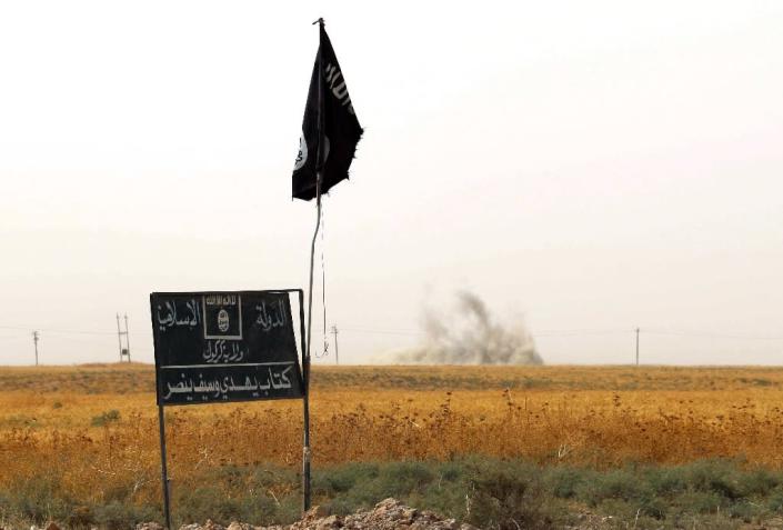 Smoke rises in the distance behind an Islamic State group (IS) flag and banner on September 11, 2015 (AFP Photo/Marwan Ibrahim )