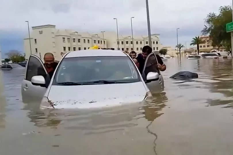 People push a stranded car along a flooded street in Dubai