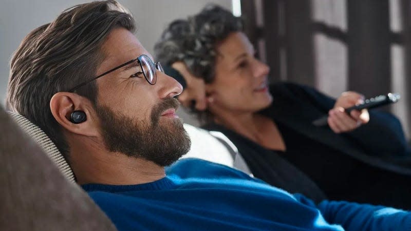 A person laying back on a sofa with a wireless earbud in their right ear.