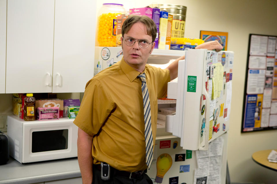 Man as TV character Dwight from "The Office" standing by an open fridge in an office kitchen