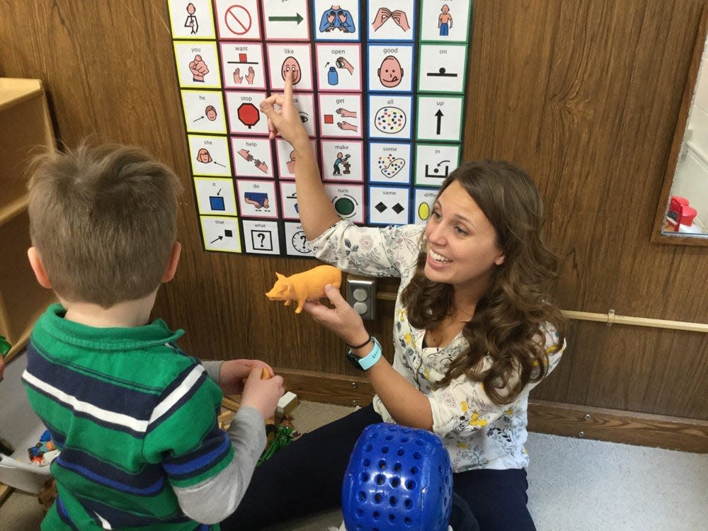 Grant Wood Area Education Agency speech language pathologist Heidi Primrose helps teach a student through play with a core board, which highlights single 'core' words that can be used alone or in combination to communicate.