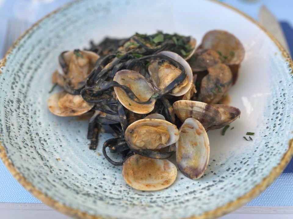 Black-colored pasta with shellfish atop it on a light blue, gold-rimmed plate at a restaurant