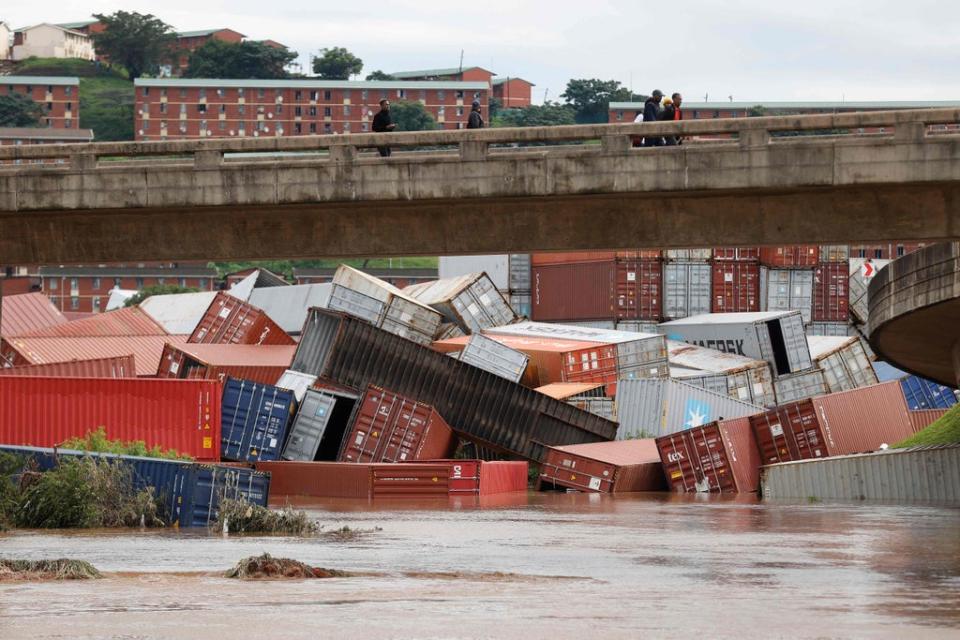 Residents of Umlazi township stand over a bridge and watch containers that fell over at a container storage facility following heavy rains and winds in Durban, on April 12, 2022 (AFP via Getty Images)