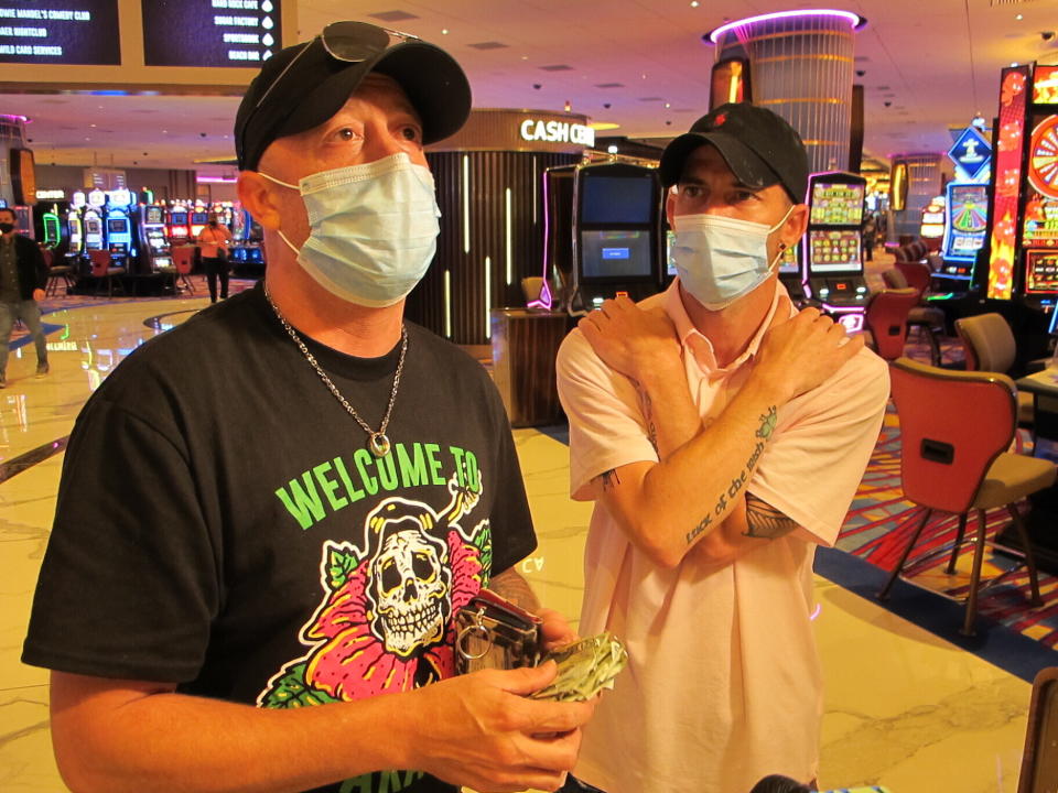 Mike McLaughlin, left, displays a wad of cash he and his friend Johnny Solis, right, planned to gamble at the Hard Rock casino in Atlantic City N.J. on July 2, 2020, the day the casino reopened amid the coronavirus outbreak. New Jersey's casinos and horse tracks won $264.5 million in July, a figure that was down nearly 21% from a year ago, but one the gambling houses will gladly take after months of inactivity. (AP Photo/Wayne Parry)